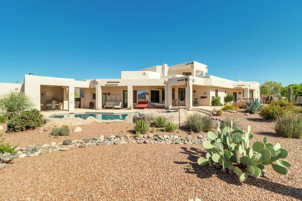 A modern two-story house with a swimming pool, surrounded by desert landscaping including cacti and agave plants.