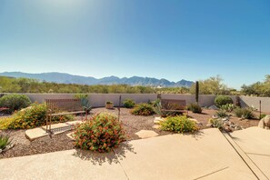 An outdoor patio with two benches, surrounded by desert plants and a view of mountains.
