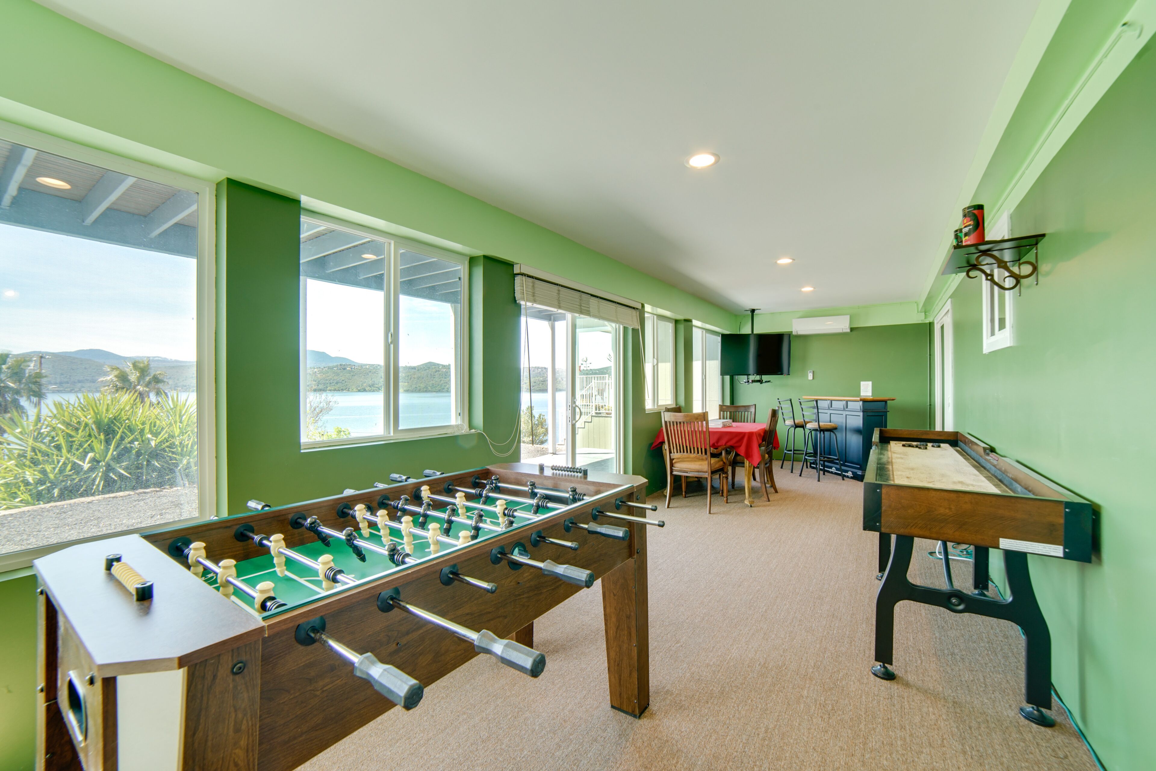 A room with a foosball table, a pool table, and a dining area with chairs and a table.