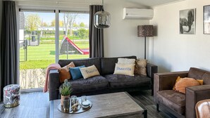Un salon avec un canapé en cuir noir, un fauteuil en cuir marron et une table basse en bois. Une fenêtre offre une vue sur un terrain de jeux et un immeuble.