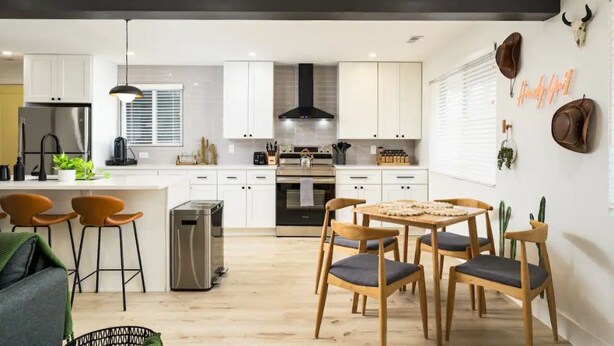 Une cuisine moderne avec des meubles blancs, un îlot central et un coin repas doté de chaises en bois.