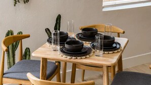 Une table à manger dressée avec des bols et des verres noirs, entourée de chaises en bois dotées de coussins gris.