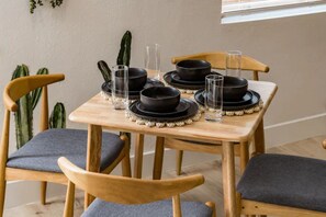 Een eettafel, gedekt met zwarte kommen en glazen, omringd door houten stoelen met grijze kussens.