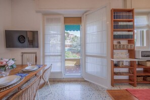 Una habitación con una mesa de comedor preparada para cuatro personas, una estantería, un televisor y vistas al exterior a través de una puerta.