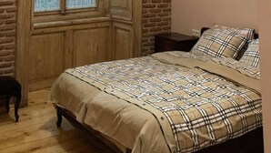Ein Schlafzimmer mit einem hölzernen Bett, einem Fenster mit Spitzenvorhängen, einer Ziegelwand und einem Deckenventilator.