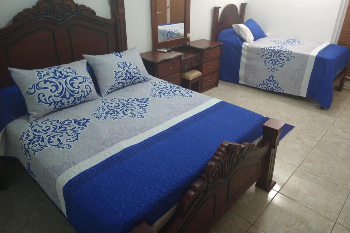 A hotel room with two beds, each with a blue and white patterned bedspread and matching pillows. There is a wooden headboard, a bedside table with a mirror, and a small wooden stool.