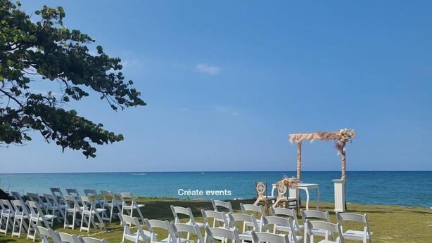 An outdoor wedding setup with white chairs arranged in rows, a small altar, and a clear view of the ocean. - Villas Rossen  (Puerto Plata)