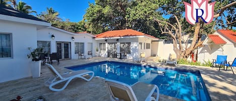 A swimming pool with lounge chairs, a patio area, and a white building with a red roof.