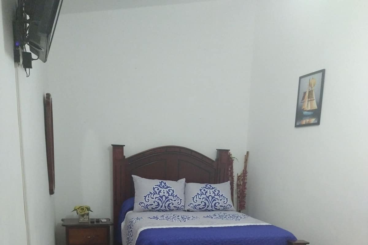 A bedroom with a wooden bed, a wicker sofa, and a small bedside table with a vase.