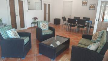 A living room with wicker furniture, a coffee table, and a dining area with chairs and a table.