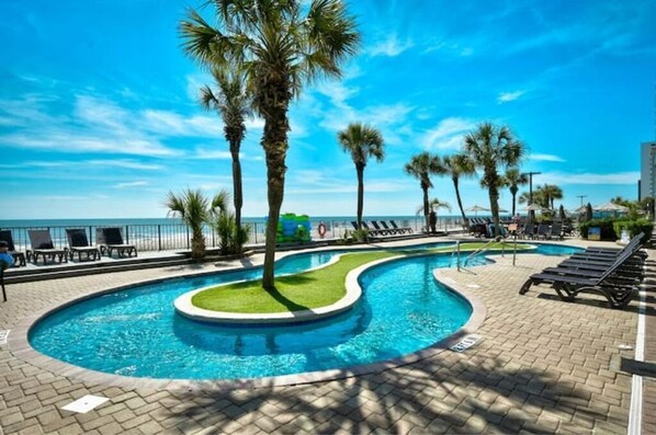 Relax by the oceanfront pool surrounded by palm trees and lounge chairs.