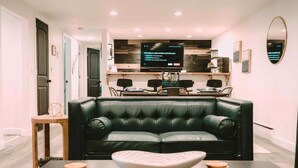 A modern living room with a dark green leather sofa, a coffee table with a decorative bowl, and a flat-screen TV mounted on the wall.
