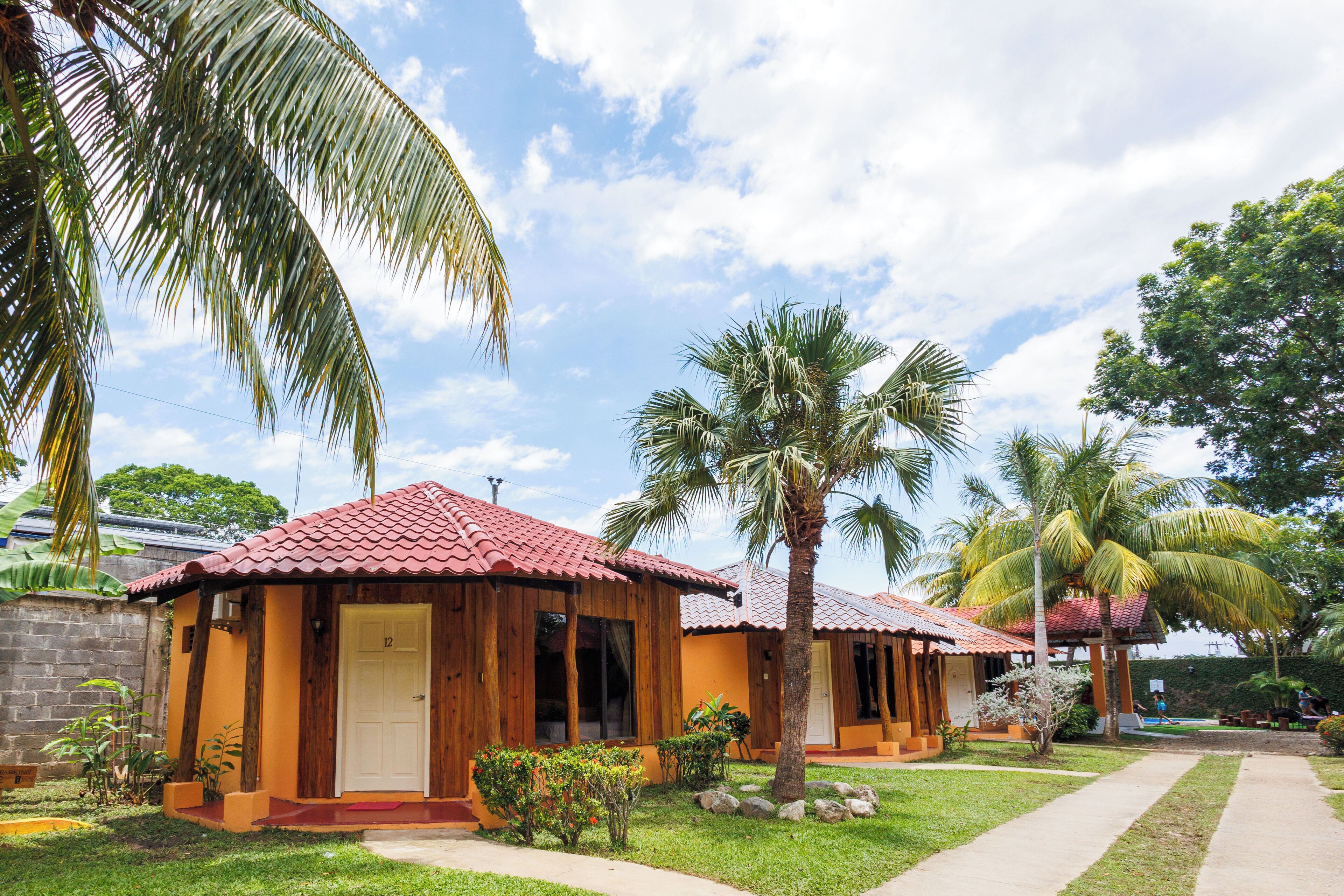 A row of wooden cabins with red-tiled roofs, surrounded by lush greenery and palm trees.