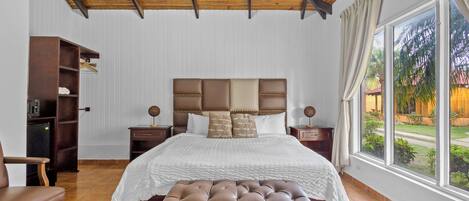 Un dormitorio con una cama grande, un banco de madera, un armario y una ventana con vistas a zonas verdes.