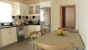 Una cocina moderna con armarios blancos, un refrigerador de acero inoxidable, un lavavajillas y una mesa de comedor de madera con sillas.