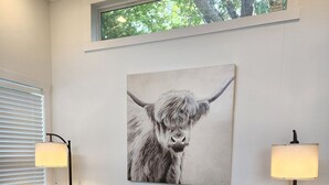 A brown leather sofa in a room with a large window, two floor lamps, and a painting of a yak on the wall. - Ranch Cabin
Modern Tiny home on beautiful Ranch! (Tyler)