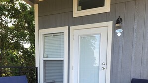 A covered porch with two blue cushioned chairs and a small table, a gray door with a window, and a wooden deck. - Ranch Cabin
Modern Tiny home on beautiful Ranch! (Tyler)