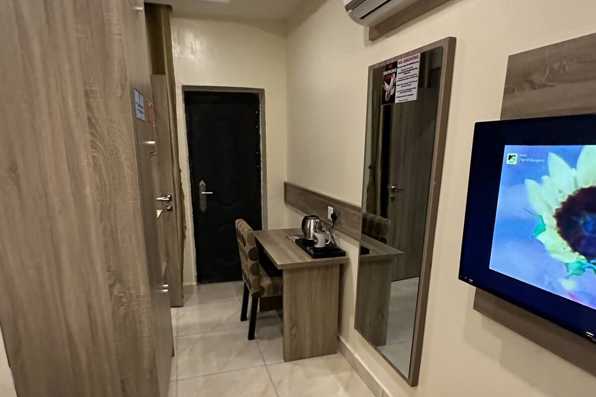 Een hotelkamer met een houten bureau, een televisie, een airconditioner en een spiegel.