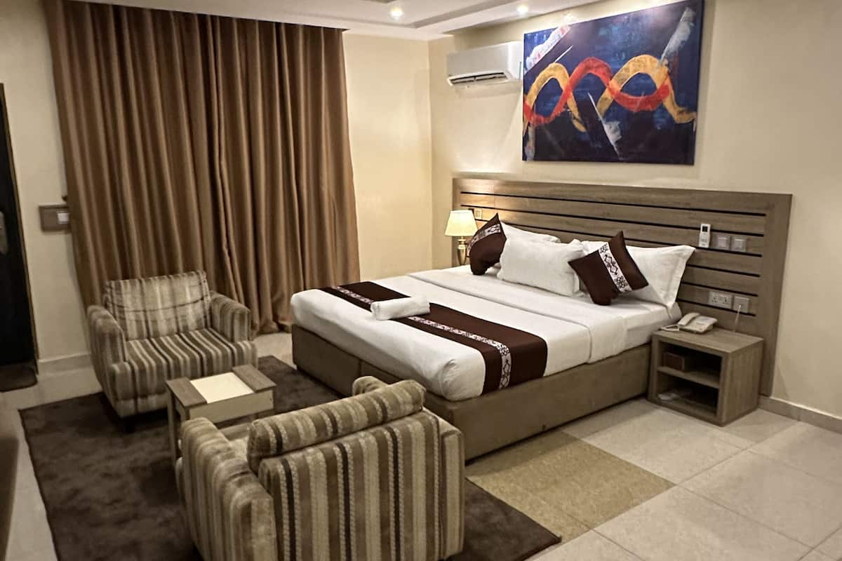 Een moderne hotelkamer met een groot bed, een bank, een fauteuil, een nachtkastje en een schilderij aan de muur.