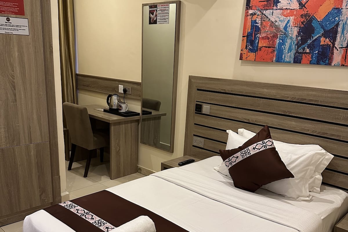 Een hotelkamer met een bed, een bureau, een stoel, een spiegel, een airconditioner en een schilderij aan de muur.