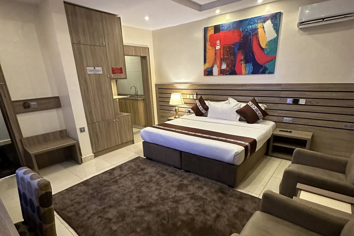 Een moderne slaapkamer met een groot bed, een zithoek met banken, een kleine tafel en een kleurrijk abstract schilderij aan de muur.