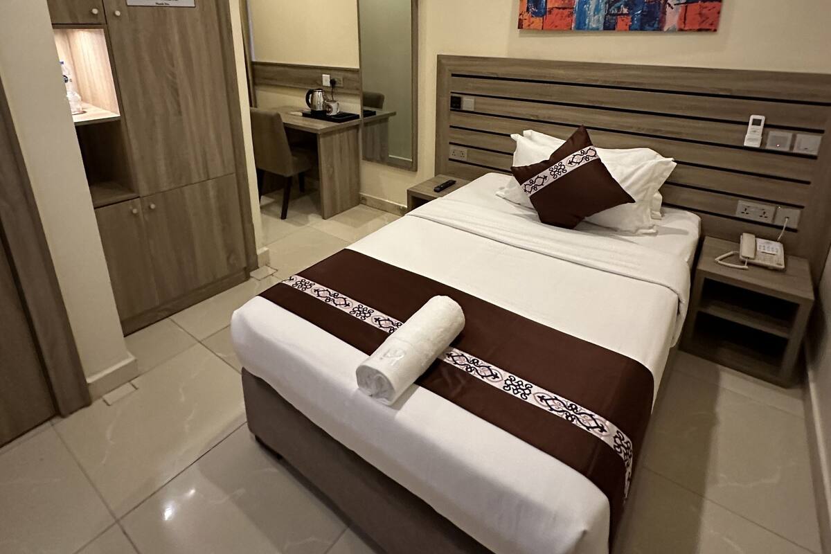 Een hotelkamer met een bed, een bureau, een stoel, een kledingkast en een schilderij aan de muur.