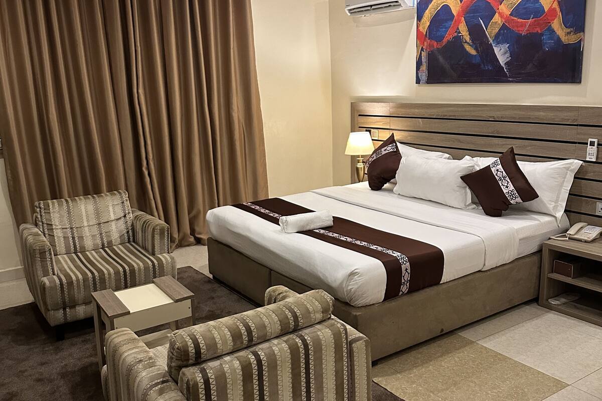 Een hotelkamer met een groot bed, een stoel, een tafeltje en een schilderij aan de muur.
