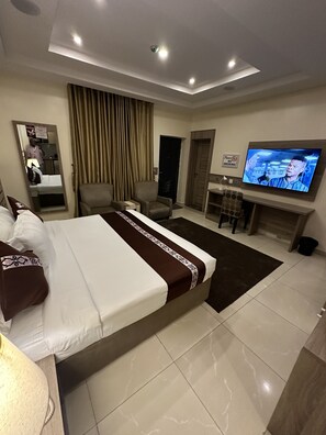 Quarto de hotel com uma cama grande, televisão, escrivaninha e uma cadeira.
