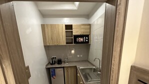 A compact kitchen with wooden cabinets, a built-in microwave, a sink, and a small refrigerator. - Moz One Executive Guest Rooms-Tourggourt (Abuja)
