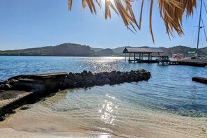 Ein klarer See mit steiniger Uferlinie, einem hölzernen Steg und einer kleinen Schutzhütte.