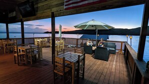 A wooden deck with tables and chairs, overlooking a body of water with a sunset view. - El Palacio Rosa - The Bay Suite (Jose Santos Guardiola)