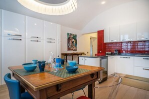 A modern kitchen with white cabinets, a red backsplash, and a dining area with a wooden table and blue chairs.