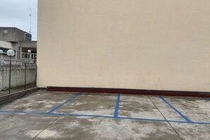 A concrete parking area with blue lines, a chain-link fence, and a building with a beige wall and a red baseboard.