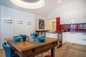 A modern kitchen with white cabinets, a red backsplash, and a dining area with a wooden table and blue chairs.