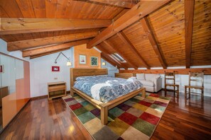 A bedroom with a wooden ceiling, a bed with a colorful rug, a nightstand, a chair, and a sofa. - GuestHost - Cozy apartment of 143 sqm, able to accommodate up to 5 people, located on the third floor of a building with lift in the heart of Udine. The location is great! In about 10 minutes walk you can reach Via Mercatovecchio, Piazza della Libertà a (Udine)