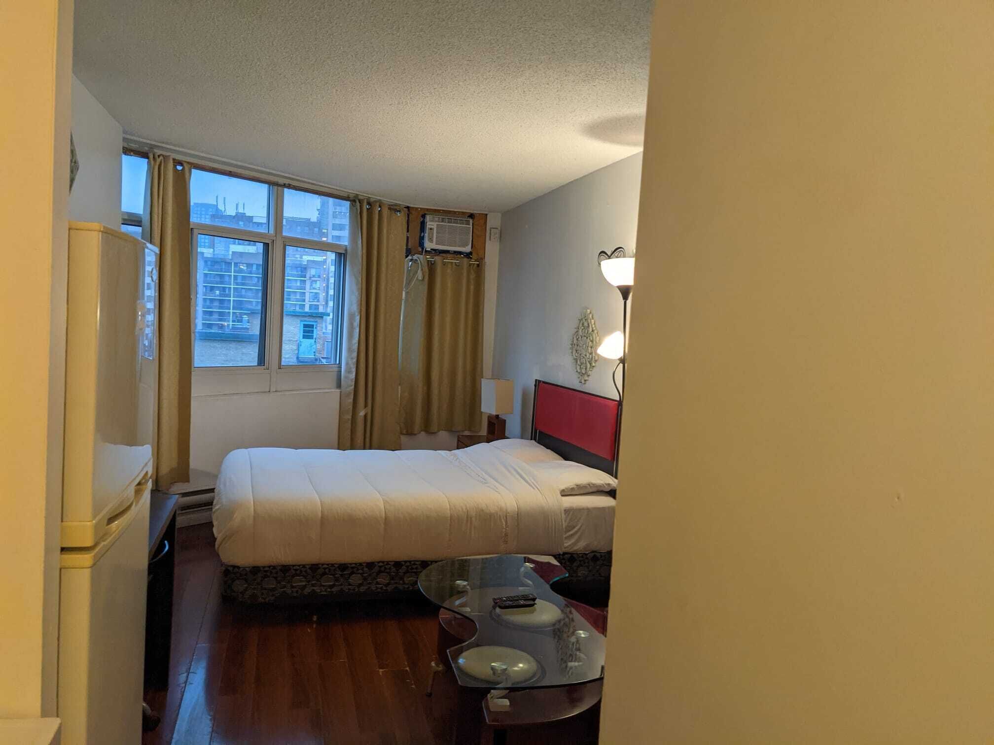A hotel room with a bed, a small table, a lamp, and a window with curtains.