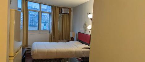 A hotel room with a bed, a small table, a lamp, and a window with curtains.