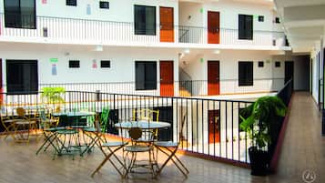 Interior de un hotel de varios niveles con balcones, mobiliario exterior y plantas en macetas.