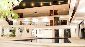 Un espacio interior de varios niveles con piscina, balcones y luces colgantes.