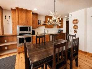 Una cocina moderna con armarios de madera, electrodomésticos de acero inoxidable, una mesa de comedor con sillas y una lámpara de techo con forma de astas.