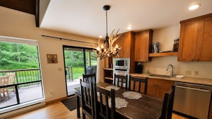 Une cuisine moderne avec des meubles en bois, une table à manger avec des chaises, un lustre et une vue sur une terrasse.