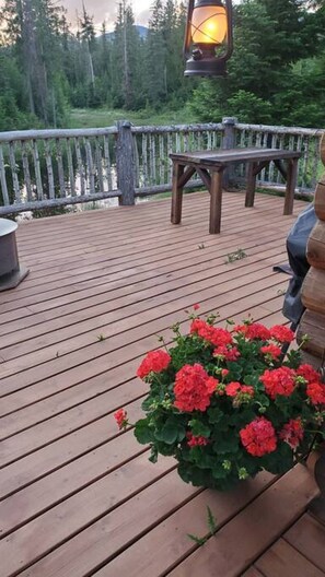 Ett trädäck med en bänk och ett bord, omgivet av ett trästaket och en blomkruka med röda blommor.