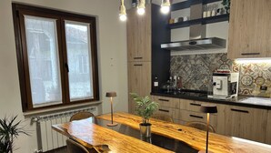 Een moderne keuken met een houten eettafel, stoelen, hanglampen en een koffieapparaat.