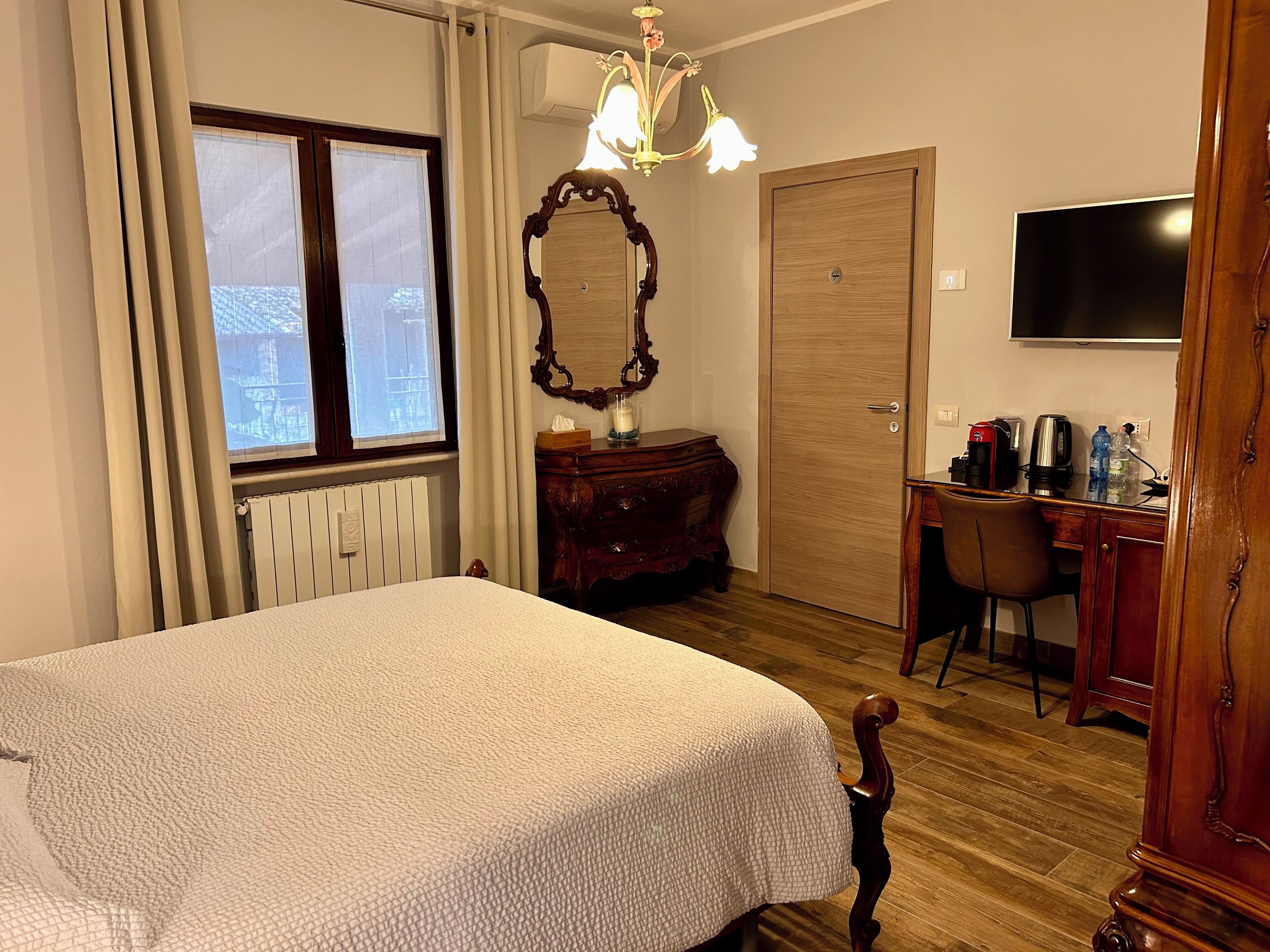 A hotel room with a bed, a desk with a chair, a television, a mirror, and a radiator.