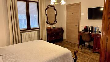 A hotel room with a bed, a desk with a chair, a television, a mirror, and a radiator.