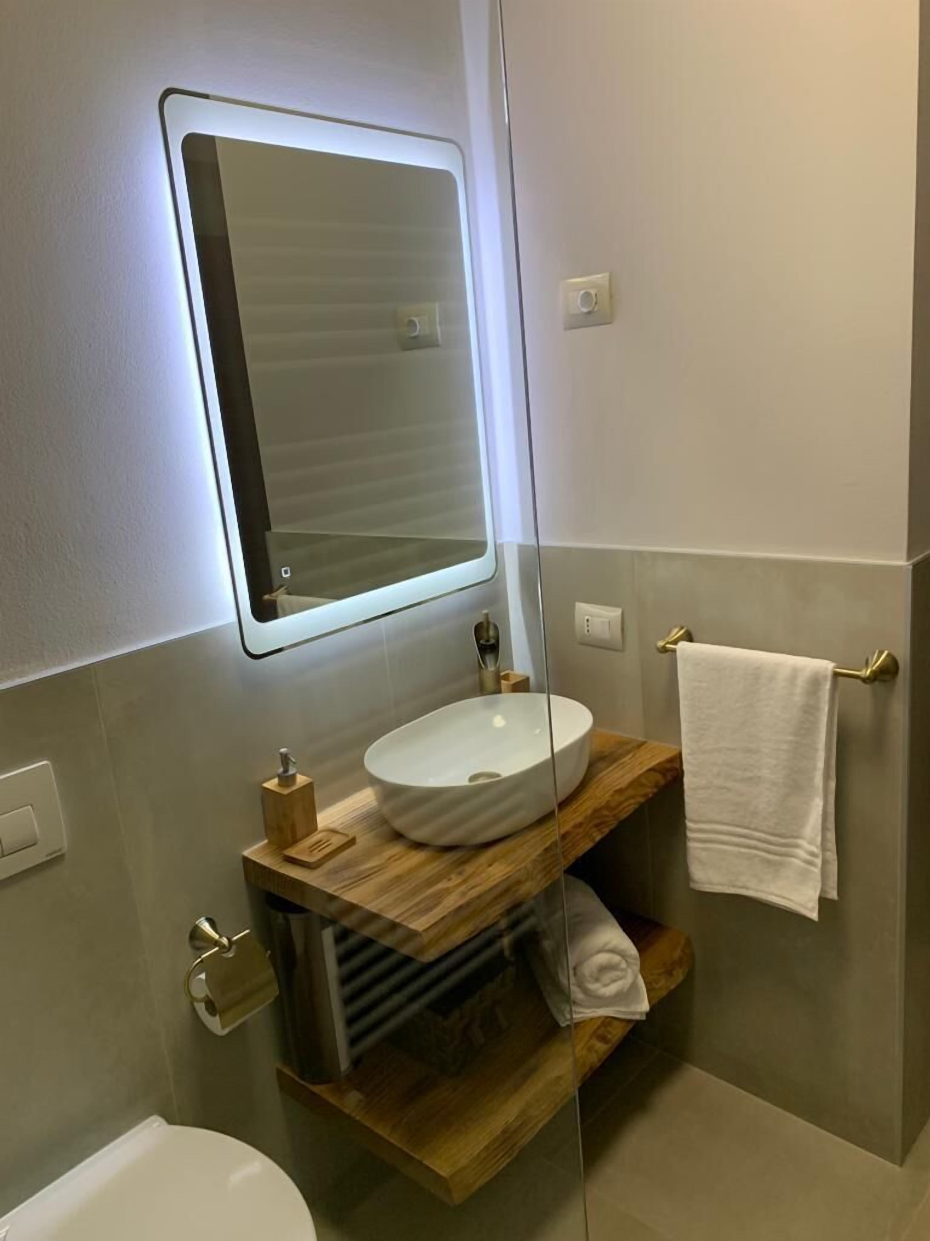 Un baño moderno con tocador de madera, un lavamanos blanco e iluminación integrada en el espejo.