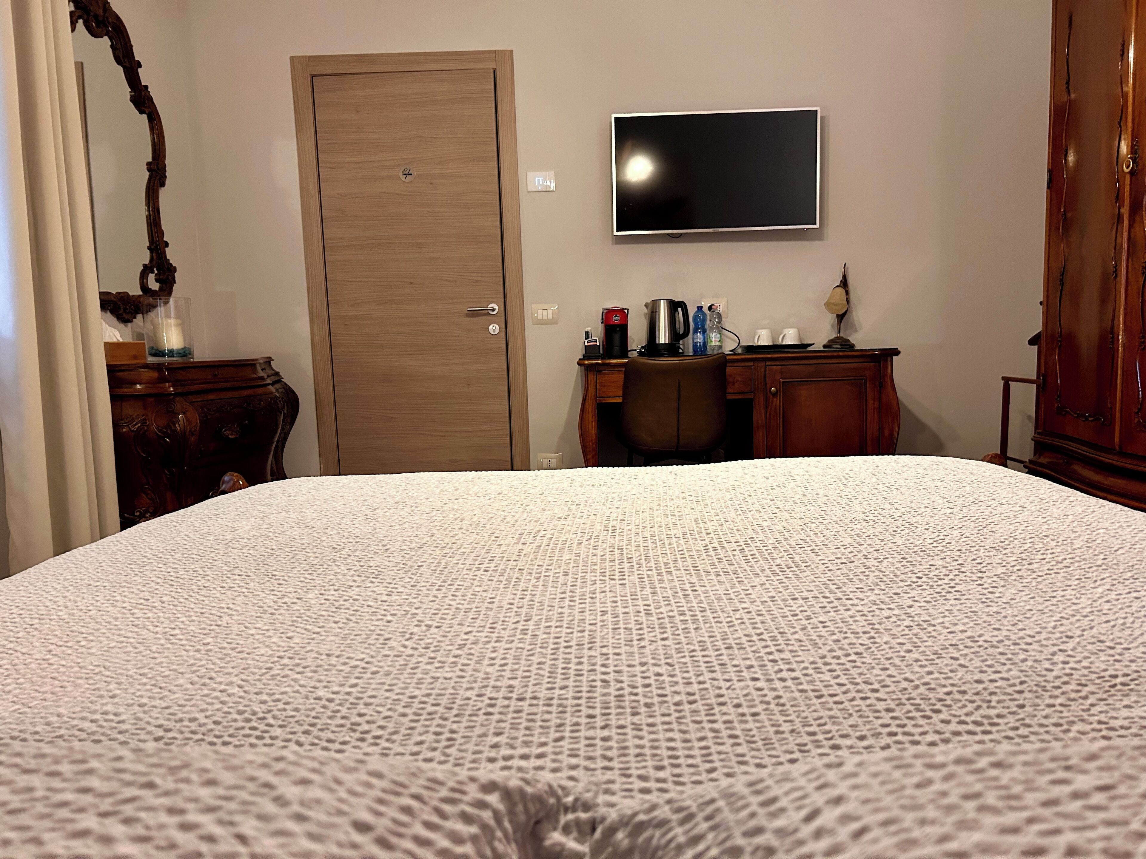 Una camera d'albergo con un letto grande, un armadio in legno, una scrivania con televisore e una macchina per il caffè.