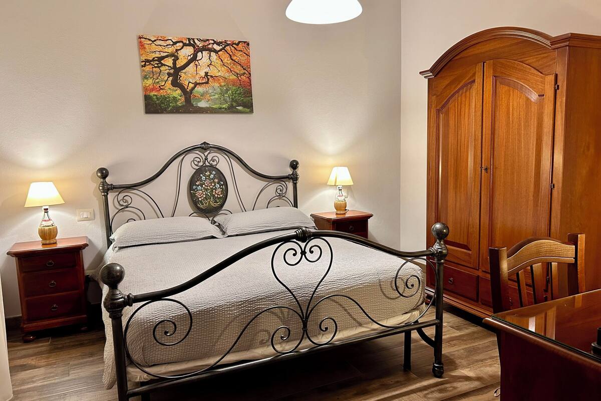 A neatly arranged bedroom with a bed, bedside tables, a wooden wardrobe, and a dining table.