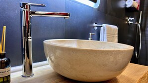 Een badkamer met een groot, rond, beige keramieken wastafel, een chromen kraan en een houten wastafelmeubel.