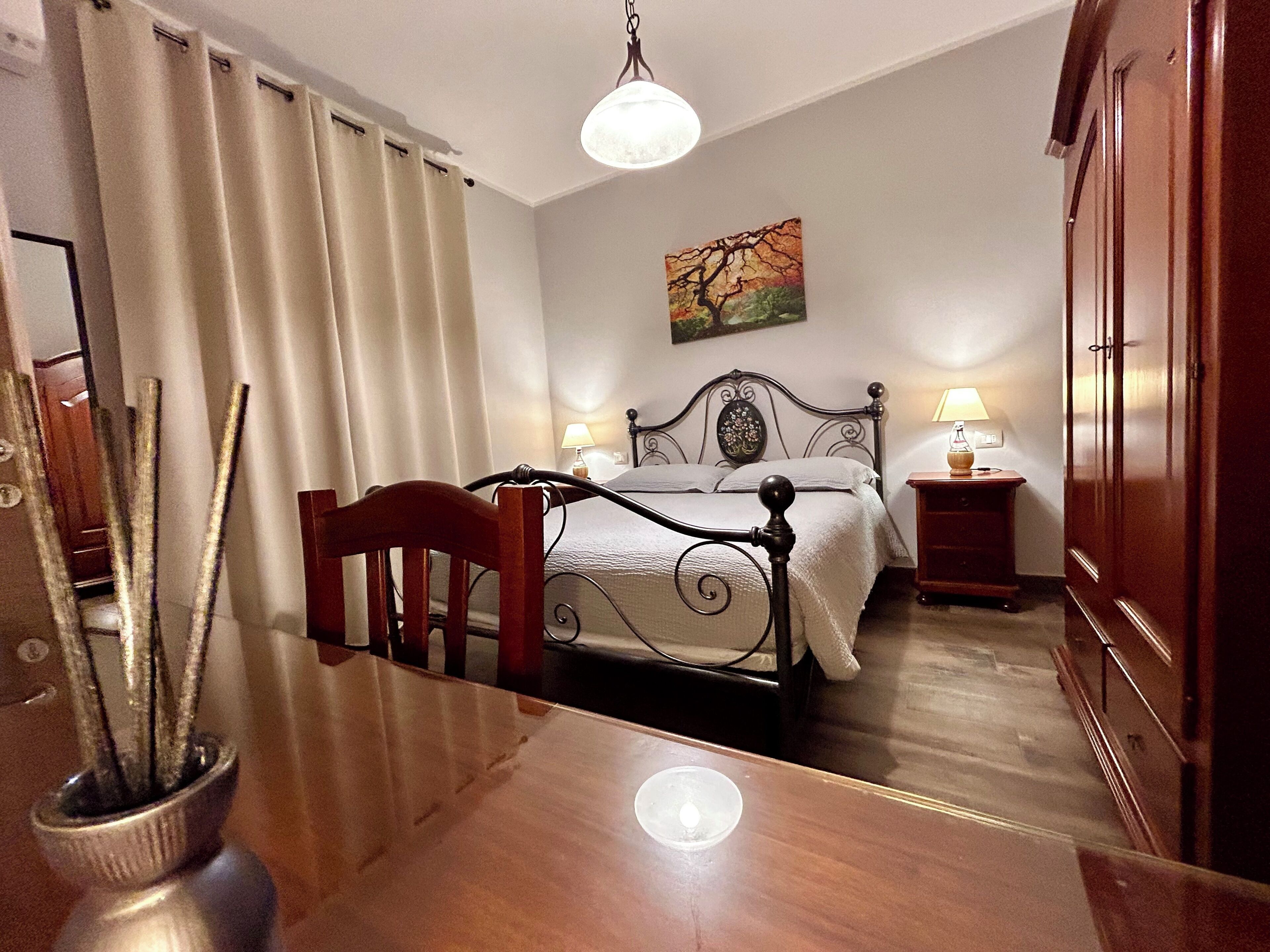 A bedroom with a wooden bed, two bedside tables with lamps, a painting on the wall, and a wooden wardrobe.